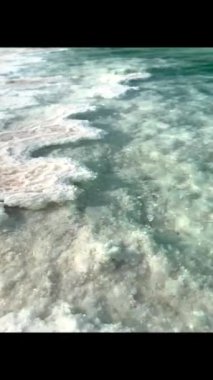 Tuz oluşumları turkuaz suyla buluşur, güneş ışığı pürüzlü dokuları parlatır. Kristal kenarlar sakin suyla birleşerek katı tuz birikintileri ile pürüzsüz yeşil yüzey arasında tezat oluşturur. Dikey video