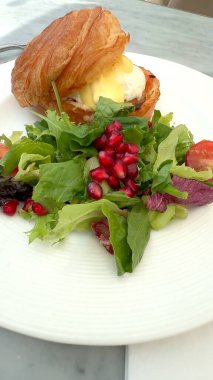  Yumurta, taze yeşillik ve nar tohumlarıyla beyaz tabakta servis edilen altın kruvasan tazelikle tatlılığı birleştiren lezzetli bir kahvaltı sunuyor. Güne mükemmel bir başlangıç.