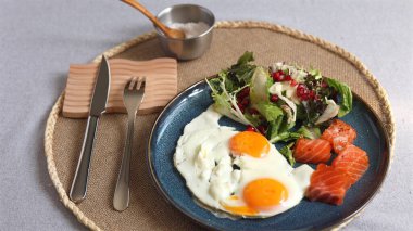 Yeşil salatanın yanında turuncu yumurtalar, nar tohumları ve mavi tabakta somon dilimleri. Ekolojik bilinçli sağlıklı yaşam tarzını vurgulayarak gümüş kase tuzla servis ediliyor..