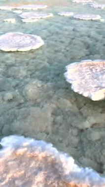 Kristal tuz oluşumları turkuaz suyla buluşur. Güneş ışığı altında pürüzsüz bir yüzeye dönüşen kaba dokular. Tuz birikintileri ve su arasındaki zıtlık huzur verici bir manzara yaratır. Dikey video