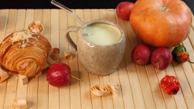  Balkabağı, kremalı sebze suyunun yanına konmuş kruvasan seramik bardakta, bambu hasırında meyveler, sonbahar hasat bolluğu, sıcak dokular, yumuşak ışık altında taze mevsimlik ürünler..