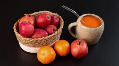 Koyu yüzeyde kırmızı elma, portakal, nar sepetinin yanında balkabağı içeceği dolu seramik kupa, taze mevsimsel ürünlere odaklanan canlı sonbahar düzeneği, kırsal cazibe, organik tonlar.