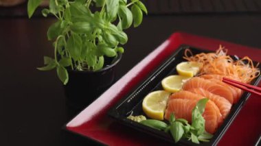 Kırmızı tabak, restoranda sashimi sunumunu geliştirir. Fesleğen ve limonla taze balık dilimleri gelişmişlik için özel kırmızı çubuklarla eşleştirilmiş görsel olarak çarpıcı bir yemek oluşturur..