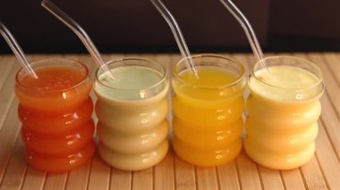 Turuncu, yeşil, sarı ve krema renginde renkli sıvılar. Tahta yüzeyde temiz pipetlerle dinleniyorlar. Parlak kurulum ferahlatıcı, doğal içecekler yaz hidrasyonu için mükemmel.