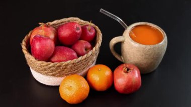 Koyu yüzeyde kırmızı elma, portakal, nar sepetinin yanında balkabağı içeceği dolu seramik kupa, taze mevsimsel ürünlere odaklanan canlı sonbahar düzeneği, kırsal cazibe, organik tonlar.