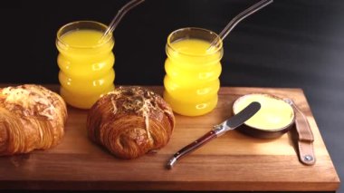 Kruvasanlar, portakallı içecekler, ahşap tahtada tereyağı taze, canlı bir kahvaltı sahnesi oluşturur. El yapımı pastalar ve soğuk içecekler güneşli bir sabahı çağrıştırıyor. 