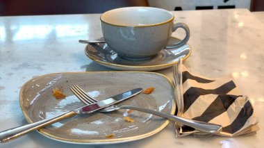 Empty gray plate rests with fork and knife, crumbs scattered after breakfast, gray cup with napkin adds texture, calm atmosphere reflects peace after breakfast, Cozy moment after breakfast. clipart