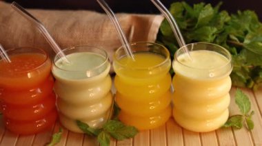 Yeşil, sarı ve krem rengi meyve suları taze nane şekeriyle çevrili ahşap tahtada pipetlerle. Canlı düzenek, temiz, çevre bilinci olan yaşam tarzı için sağlıklı ve ferahlatıcı içecekler sunuyor..