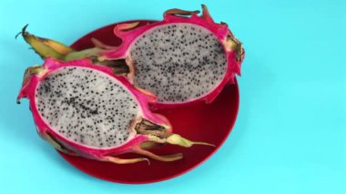 Dilimlenmiş organik ejderha meyvesi mavi arka planda canlı kırmızı plakaya siyah tohumlu benekli beyaz et ortaya çıkarır. Eko sunumu organik tazeliği ve canlı renkleri vurguluyor.