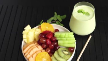  Kavanozda renkli meyveler ananas, kivi, kavun ve çilek, yanında eko içecek, koyu arkaplanda yeşil ve turuncu renkler meyve uyumu sembolü, eko sağlık kavramı.