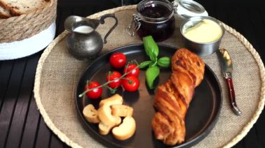 İçinde siyah tabak, taze vişneli domates, tereyağlı pasta ve kaju fıstığı olan rahat bir kahvaltı. Kremalı ve otlu gümüş sürahi sağlıklı, basit bir sabah rutinini çağrıştırıyor..
