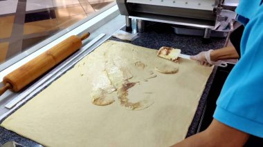 Eldivenli eller profesyonel mutfakta hamuru tarçınla dolduruyor, mükemmel tarçın ruloları için gereken dikkatli hazırlıkları vurguluyor, hatta yayılma ve hassasiyeti vurguluyor..