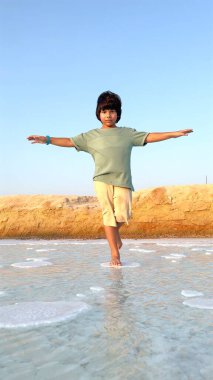 Çocuk tuz parçacıkları üzerinde, dağılmış tuz oluşumları ve kristal berrak suyla çevrili gevşek bir ifadeyle denge kurarak macera ve doğal güzelliğin neşeli bir sahnesini yaratır.. 