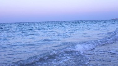 Yumuşak beyaz armalı okyanus dalgaları, şafak öncesi renklerle bezenmiş kumlu sahille buluşup güneş doğmadan önce huzuru çağrıştıran sakin bir manzara yaratıyor. Sabah sakin konsept.