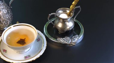 Klasik gümüş çatal bıçak ve şeker kabıyla eşleştirilmiş narin çiçekli fincanda servis edilen kahvaltı çayı sonsuz zarafet yayar. Sıcak tonlar ve ince detaylar klasik cazibeyi artırır.