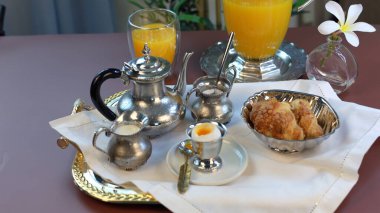 Breakfast table with vintage silverware. classic setup embraces nostalgic charm. Fresh juice, croissants, boiled egg, small jacks with milk, sugar add vibrant contrast to serene ambiance  clipart