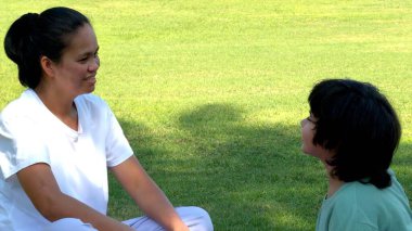Anne-çocuk çimenler üzerinde oyunculuk egzersizi yapıyor, aktif hareketlerle gülümsüyor, güneş ışığı spor salonuna, aile refahına, açık hava aktivitelerine odaklanıyor..