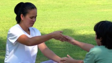 Anne ve çocuk çimenler üzerinde eğlenceli bir egzersiz yapıyor, aktif hareketler yoluyla gülümsüyor ve kaynaşıyor, güneş ışığı açık hava sporları ve aile refahı, sağlıklı yaşam konseptine odaklanıyor..