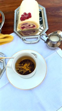 Bardağın yanında meyveli kek, süslü tepside dinlenen kremalı pasta. Kupa ve pasta, bereketli bahar manzarası altında canlı bir tropik cazibe getirir. Tatlı ziyafeti konsepti.