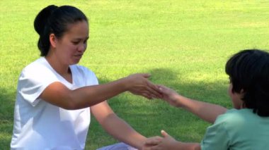 Anne ve çocuk çimenler üzerinde eğlenceli bir egzersiz yapıyor, aktif hareketler yoluyla gülümsüyor ve kaynaşıyor, güneş ışığı açık hava sporları ve aile refahı, sağlıklı yaşam konseptine odaklanıyor..