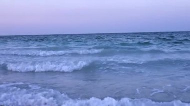 Günün ilk ışıklarıyla kumlu sahilde beyaz köpüklü dalgalar yavaşça süzülür. Sahildeki yeni günün yumuşaklığını yansıtır. Okyanus durgunluğu kavramı.