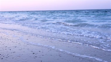 Foamy ocean waves softly caress golden sand under sky beginning to glow with morning colors, creating sense of quiet anticipation for day to come. Dawn tranquility concept. clipart