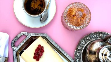 Cake arranged with swirls next to coffee cup on pink surface, crystal jar, polished silver adding refined table design. Coffee cup highlights cake visual charm. Overhead display concept. clipart