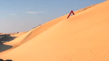 Yol işareti, doğanın gücünü sembolize eden çöl kumuyla kısmen gizlenmiş. Bölgeyi kaplayan altın kumlar engin ve kurak arazide yol işaretlerini harmanlıyor. Kum hareketi bu sahneye hükmediyor..