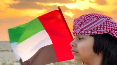 Emirati çocuğu, miras ve birliği simgeleyen BAE bayrağını gururla taşıyor. Emirati çocuğu, bu güçlü Emirati gösterisinde bayrak sallayarak, ulusal gururu yansıtan, dimdik ayakta duruyor. 