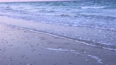 Beyaz köpükle kaplanmış yumuşak dalgalar gökyüzünün altındaki kumların üzerine süzülüyor. Sabah erken ışıklarıyla boyanıyor. Huzurlu ve nazik bir güzellikle dolu bir sahne sunuyor. Yumuşak şafak konsepti.