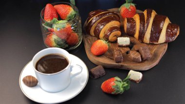 Kahvaltı masası taze çilek ve çikolatalı kruvasanlarla çevrili kahve fincanları ile parlıyor, kahve ve çikolatanın cesur zenginliğini meyve aksanıyla birleştiriyor. Yemek kampanyaları için ideal.