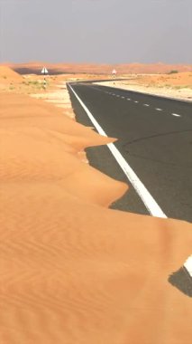 Kum kayması ile kaplı çöl yolu, doğanın alanı geri kazandığına dair çarpıcı görüntüler yaratır. Rüzgârlı kum, çöl arazisine hükmediyor. Altın yabana giden yolları harmanlıyor. Doğal ıslah sembolü.