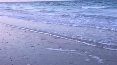 Beyaz köpükle kaplanmış yumuşak dalgalar gökyüzünün altındaki kumların üzerine süzülüyor. Sabah erken ışıklarıyla boyanıyor. Huzurlu ve nazik bir güzellikle dolu bir sahne sunuyor. Yumuşak şafak konsepti.