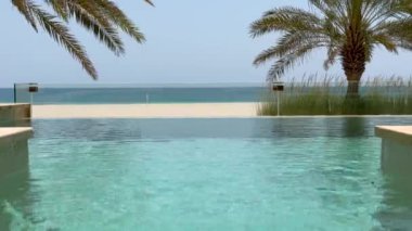 Turkuaz yüzme havuzu. Parlak su ve mavi okyanusla çevrili lüks turistik bir tatil köyünde. Sakin palmiye ağaçları ve palmiye yaprakları huzurlu bir yaz rahatlama noktası oluşturur...