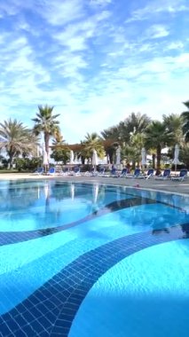 Havuz kenarında dinlenme yeri, sakin palmiye ağaçları, güneş ışığını yansıtan köpüklü su, dinlenmek ve dinlenmek için havuz kenarı cenneti yaratıyor.