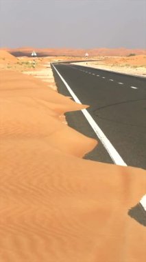 Kum kayması ile kaplı çöl yolu, doğanın alanı geri kazandığına dair çarpıcı görüntüler yaratır. Rüzgârlı kum, çöl arazisine hükmediyor. Altın yabana giden yolları harmanlıyor. Doğal ıslah sembolü.