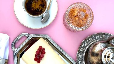 Cake arranged with swirls next to coffee cup on pink surface, crystal jar, polished silver adding refined table design. Coffee cup highlights cake visual charm. Overhead display concept. clipart