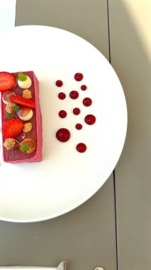 Çilekli pembe köpüklü tatlı süs böğürtlenli beyaz bir tabakta duruyor. Narin dokuları, taze aromaları ve sanatsal kaplamayı vurguluyor. Rafine tatlı armoni konsepti.