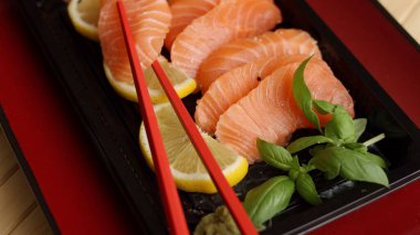 Canlı kırmızı tabakta servis edilen saşimi zarif bir yemek deneyimi yaratır. Taze fesleğen, limon dilimleri tat dengesini sağlarken, özel kırmızı çubuklar modern sofistike bir dokunuş ekliyor..