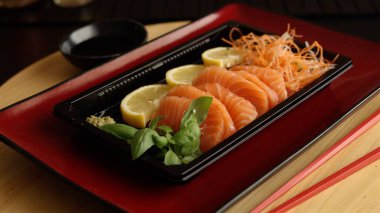 Sashimi served on vibrant red plate brings touch of elegance to restaurant experience. Fresh lemon and basil add brightness while soy sauce and red sticks create perfect balance of tradition and taste clipart