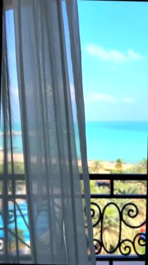 Perdeler kıyı balkonunda sallanıyor, uzak kıyı balkonları mavi sulara bakıyor, perdeler yumuşuyor, ferahlatıcı hava otel odasını dolduruyor, işten sonra dinlenmek için mükemmel bir otel.