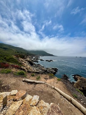 Mavi okyanusta gri kayalıklı yeşil dağlar