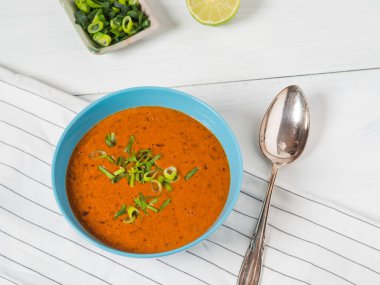 Beyaz ahşap bir masada limonlu taze domates çorbası ve taze soğan.