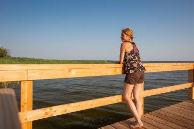 Bir rıhtımda duran, yan bakan, rahatlatıcı olgun bir kadının arka görünüşü - Mecklenburg Vorpommern, Almanya - uzayı kopyala