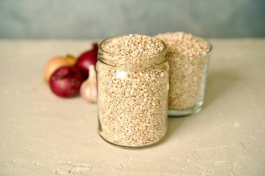 A glass jar filled with pearl barley on a light surface.