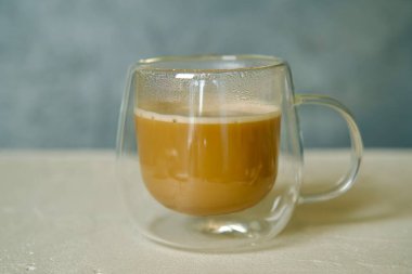 A minimalist composition featuring a cup of instant coffee in a transparent double-walled mug, placed on a light textured surface. clipart