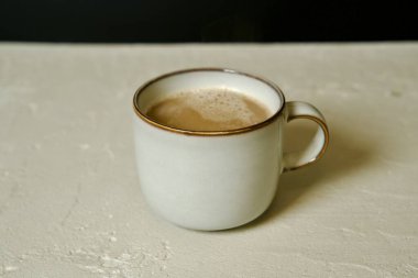 Hafif desenli bir yüzeye yerleştirilmiş gri seramik bardakta bir fincan hazır kahvenin yer aldığı minimalist bir kompozisyon..