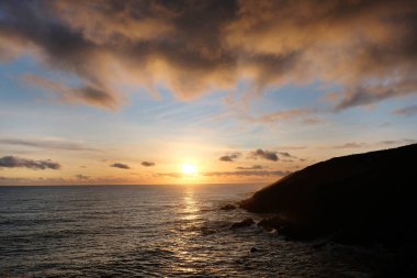 Sahilde gün batımı, güneşe karşı karanlık dağ