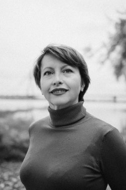 Sonbahar yapraklarıyla çevrili, parktaki olgun bir kadının neşeli portresi. O parlak kırmızı bir balıkçı yaka kazak giyiyor. Açık havadan hoşlanmakla ilgili konular için mükemmel, orta yaş, mevsimsel değişim, ve kaygısız anlar..