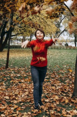 Parkta yürüyen bir kadın. Arka planda altın yapraklı ağaçlar yer alıyor ve rahat ve doğal atmosfere ekleniyor. Bu fotoğraf sonbaharın güzelliğini mi yansıtıyor? Doğanın basit zevkleri için mutluluk, rahatlama ve takdir duygusu verir.